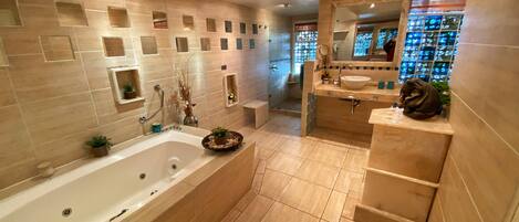 A modern bathroom with a large bathtub, a vanity with a sink, and a mirror. There are multiple shelves with toiletries and a decorative plant on the vanity.