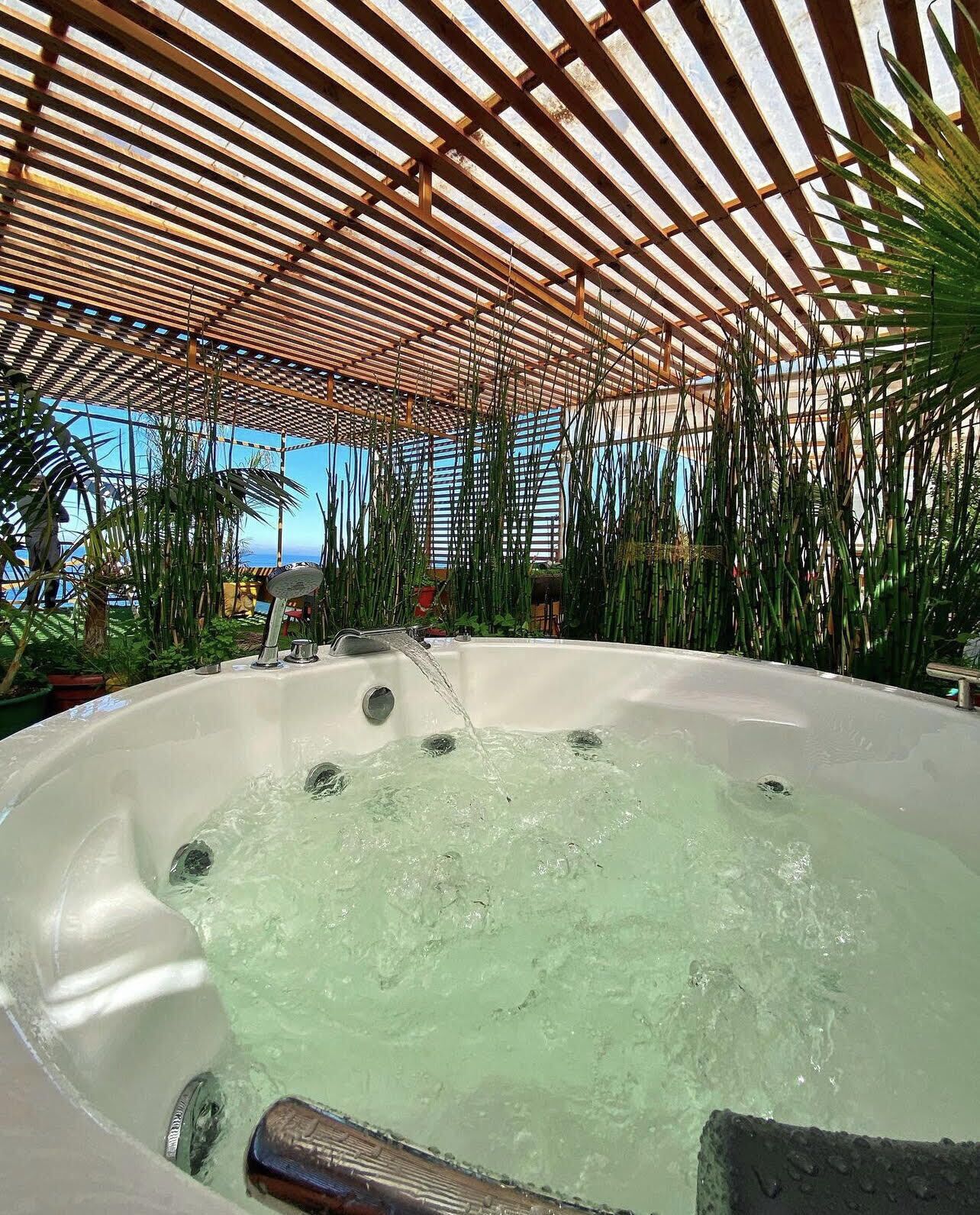 Ein Whirlpool unter einer Holzpergola, umgeben von Pflanzen.