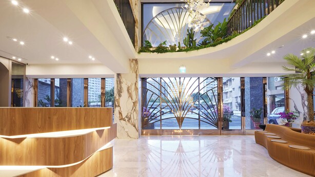 Un moderno vestíbulo de hotel con un mostrador de recepción curvo, un separador de vidrio central y vistas a la ciudad.