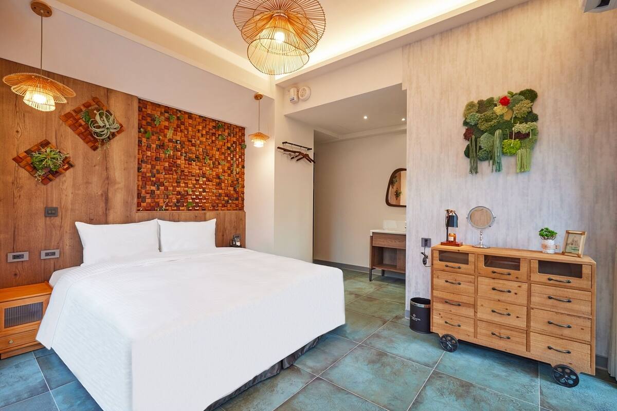 A modern bedroom with a large bed, wooden wall paneling, a wooden dresser, and a wall-mounted plant arrangement.