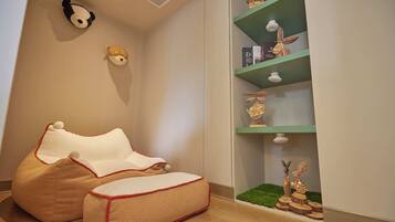 Una habitación acogedora con un sillón orejero, una estantería con adornos y un peluche de panda en la pared.
