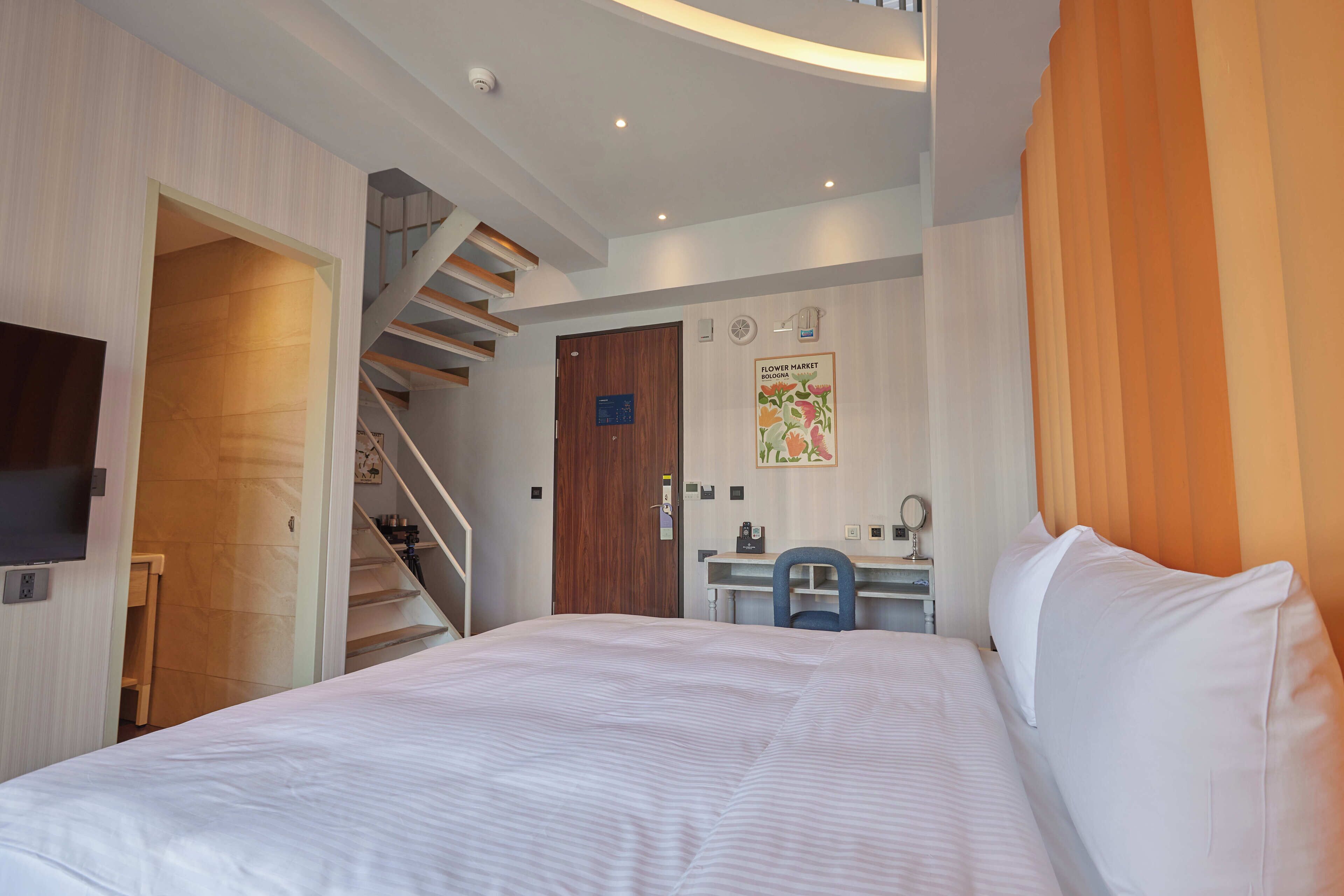 A bedroom with a bed, a desk, a chair, a wooden door, and a staircase.