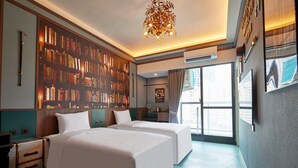 Habitación de hotel con dos camas, una estantería, una araña y vistas a la ciudad.