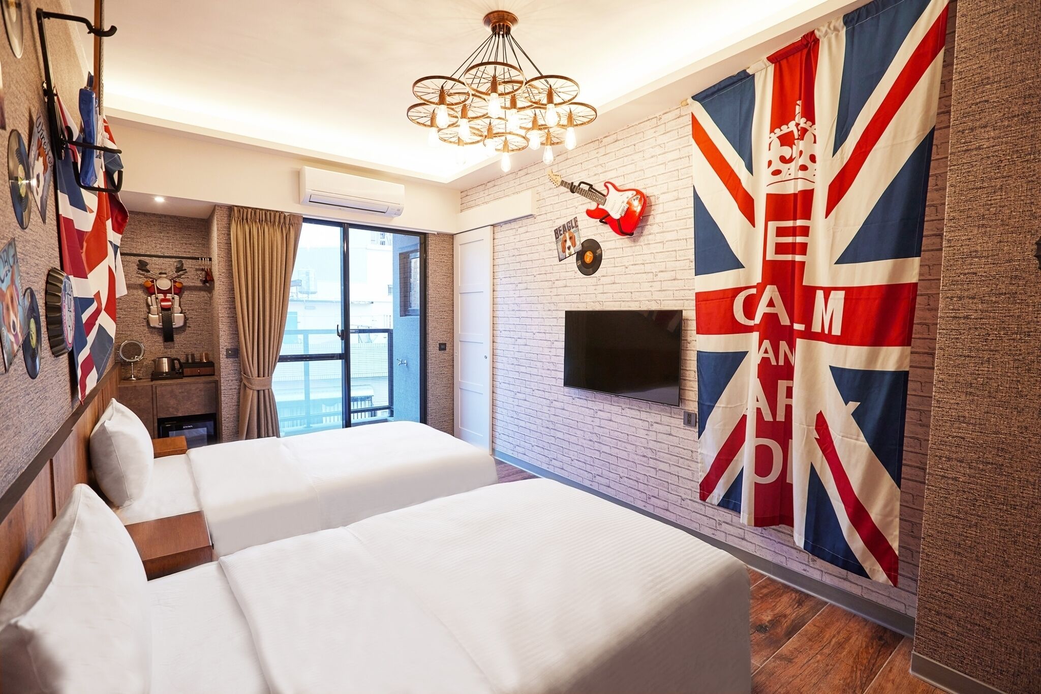 Une chambre d’hôtel avec deux lits, un téléviseur à écran plat, un mur en briques et un grand drapeau Union Jack.