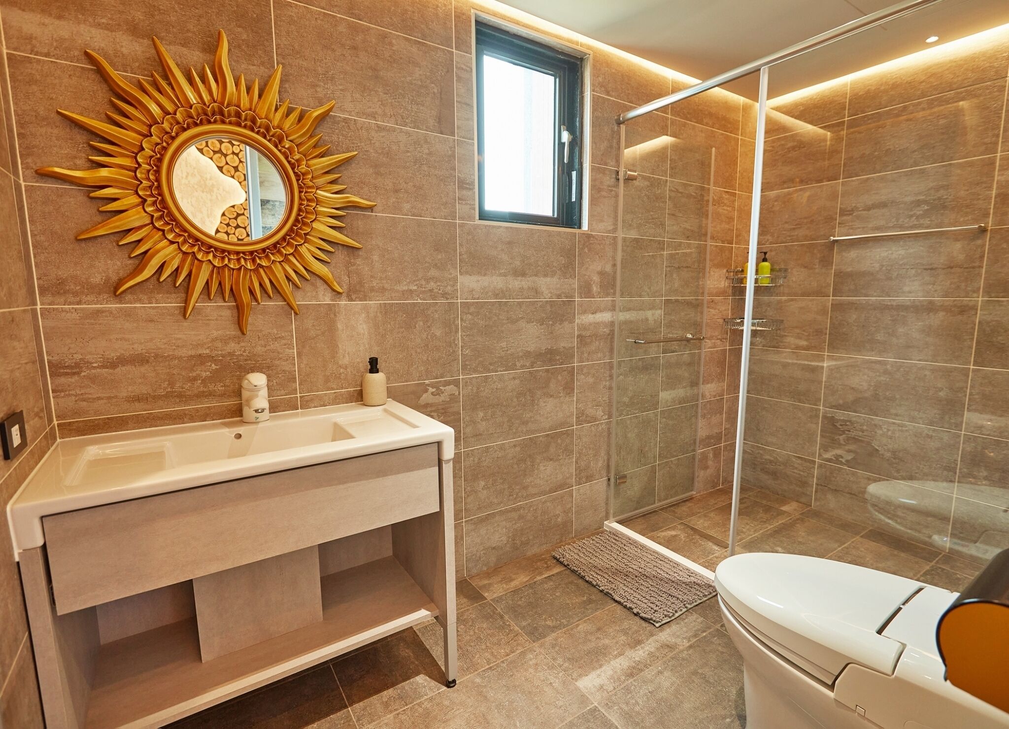 A bathroom with a sunburst mirror, a shower, and a toilet.