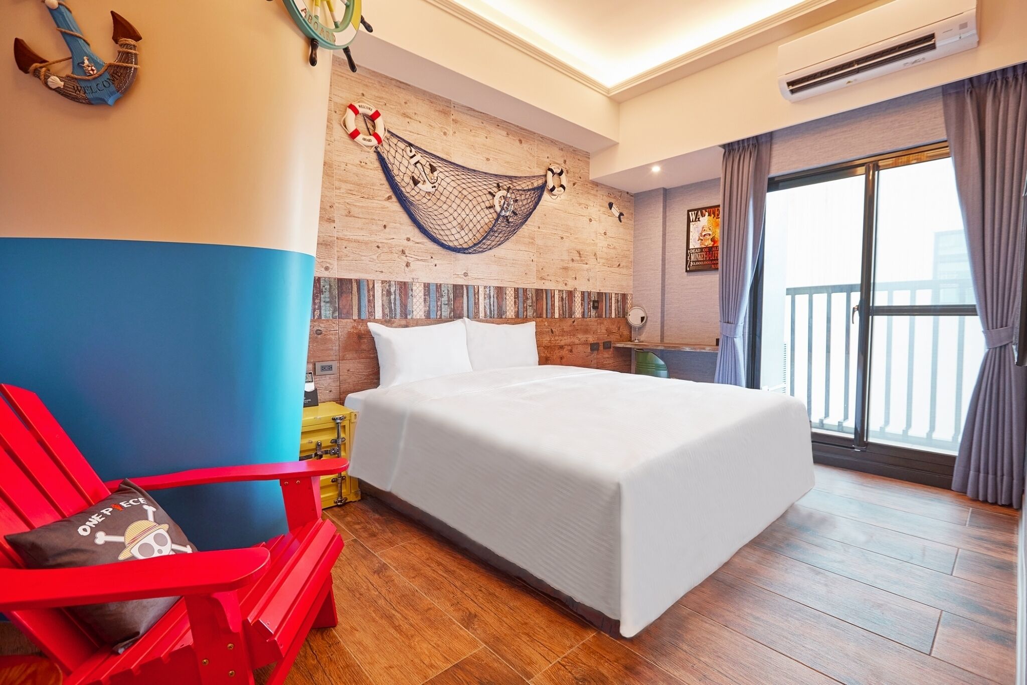 A hotel room with a large bed, a red chair, a hammock, and a balcony with curtains.