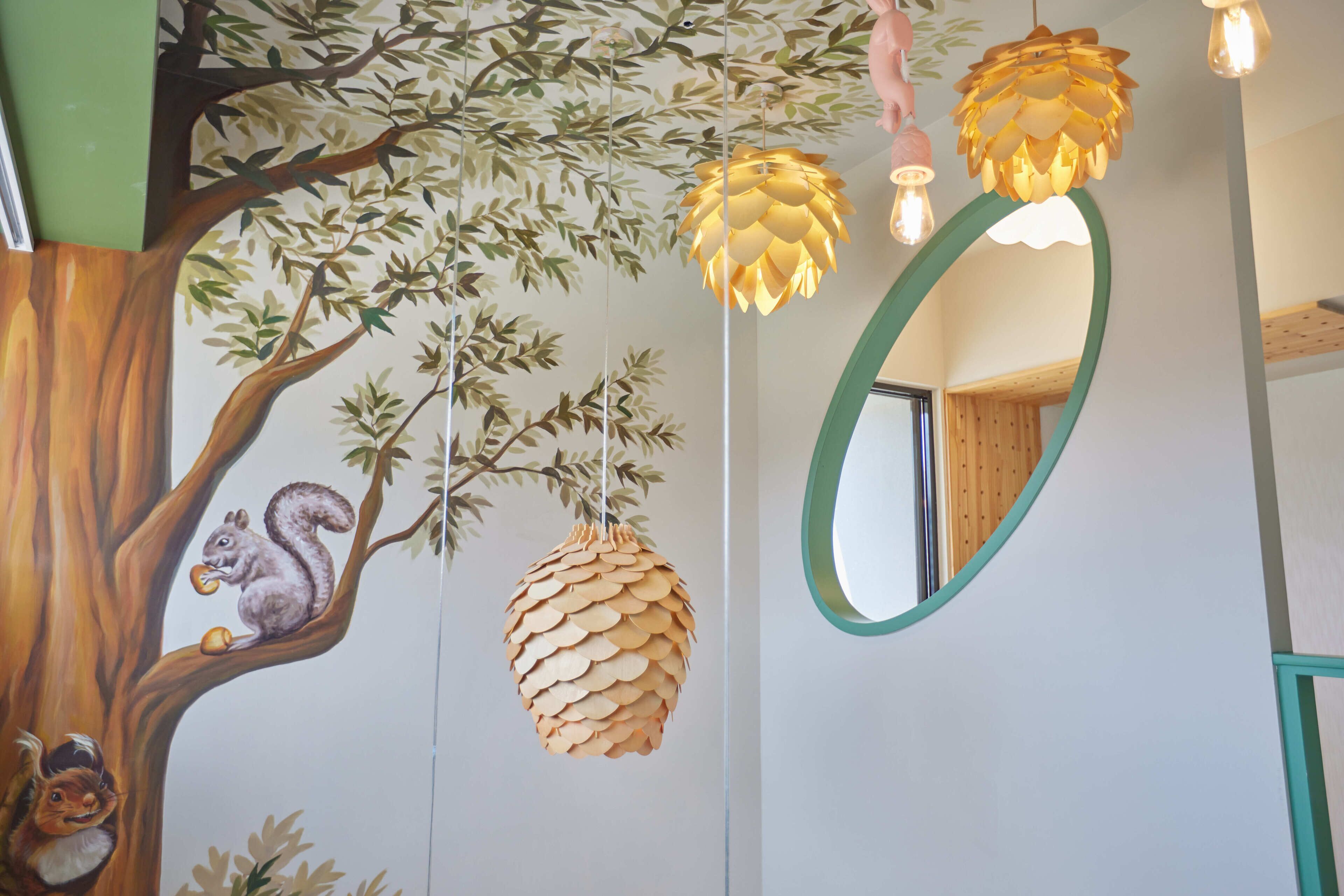 A wall with a tree mural, hanging pinecone decorations, and a mirror.