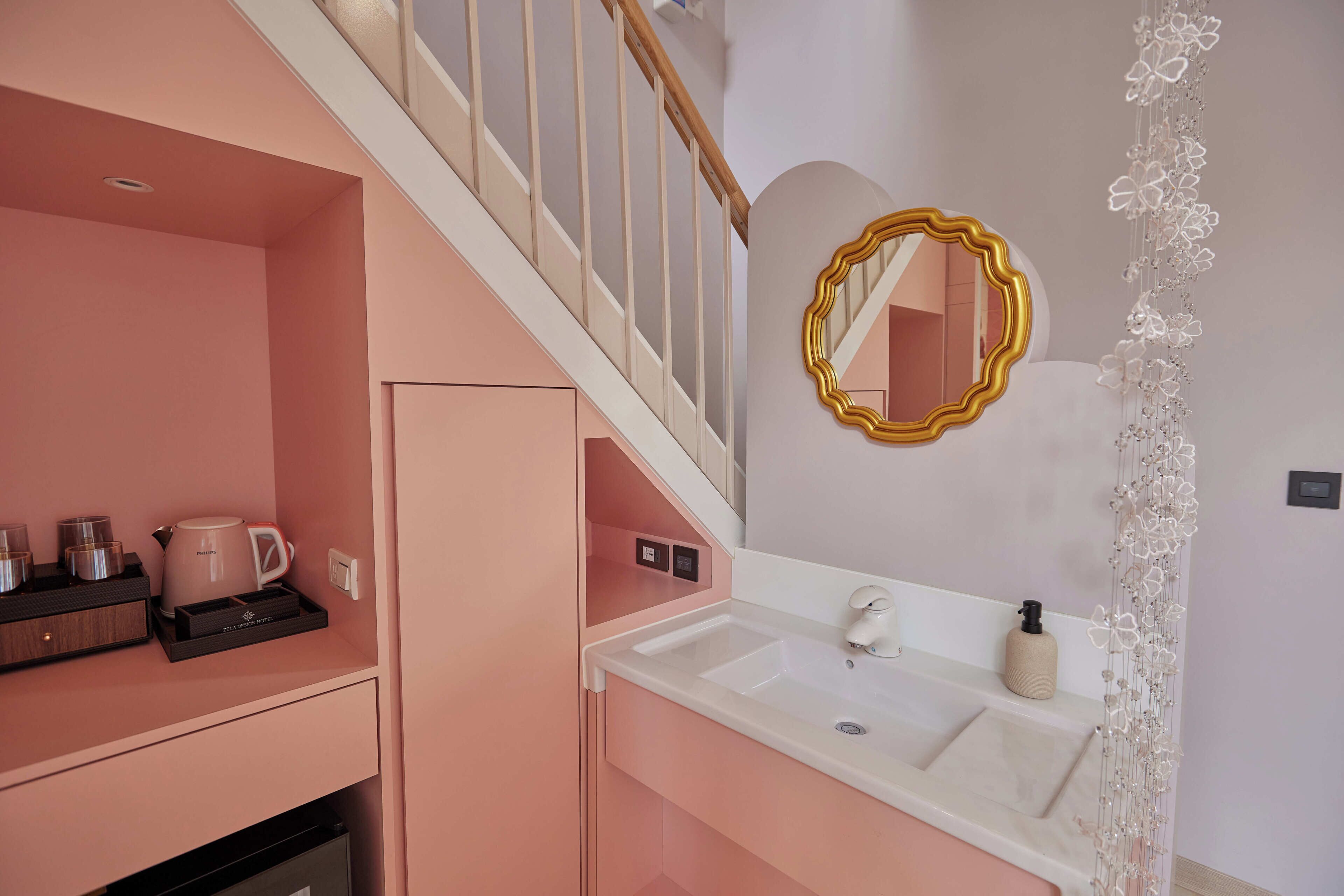 Un baño con decoración rosa, un lavamanos blanco, un espejo con marco dorado y un arreglo floral decorativo.