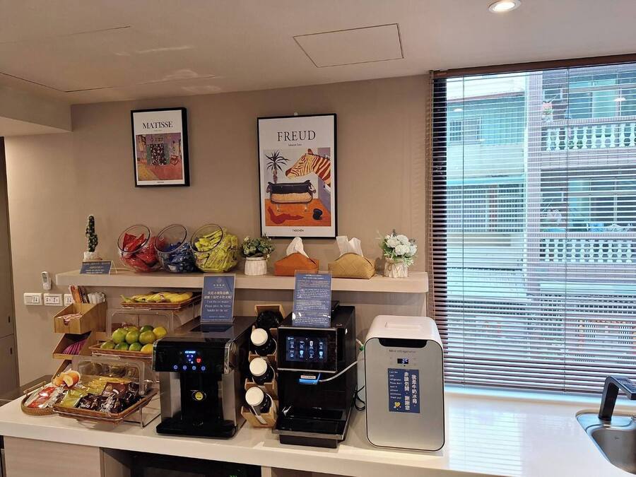 A hotel reception area with a coffee station, a mini-refrigerator, and various amenities like a fruit basket and a small plant.