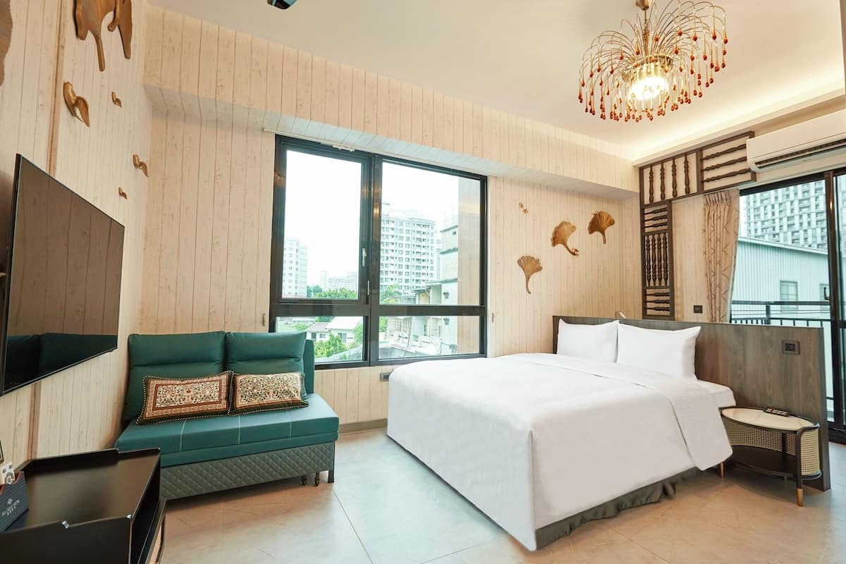 A modern hotel room with a large bed, a green sofa, a TV, and a city view.