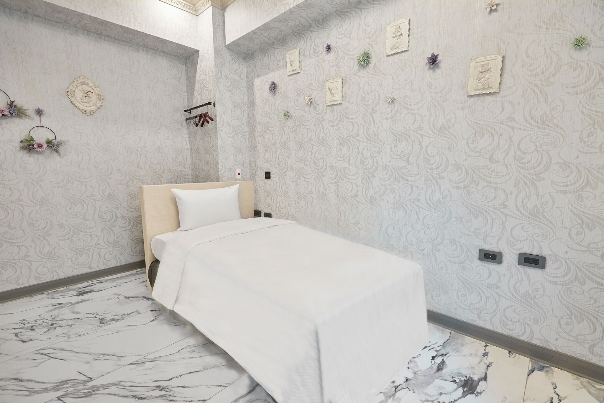 A neatly arranged bedroom with a single bed, patterned wallpaper, and a marble floor.