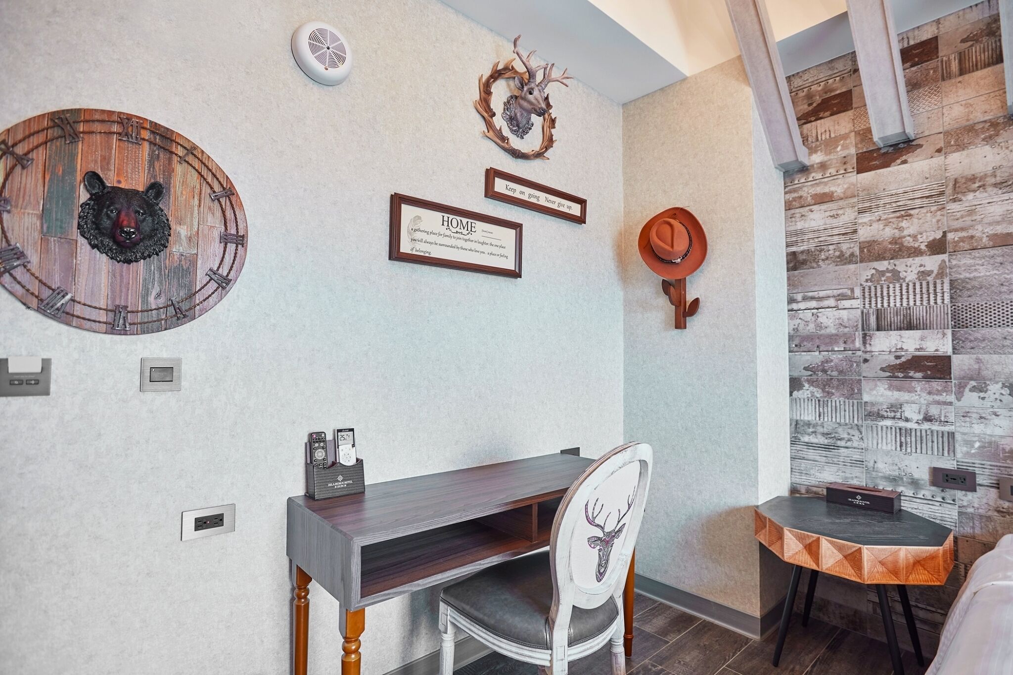 A room with a wooden clock, a framed quote, a deer head wall decoration, a small table, and a chair.