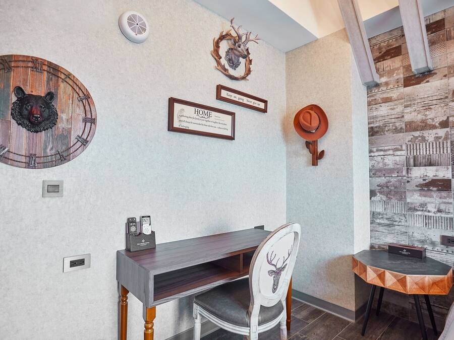 A room with a wooden clock, a framed quote, a deer head wall decoration, a small table, and a chair.