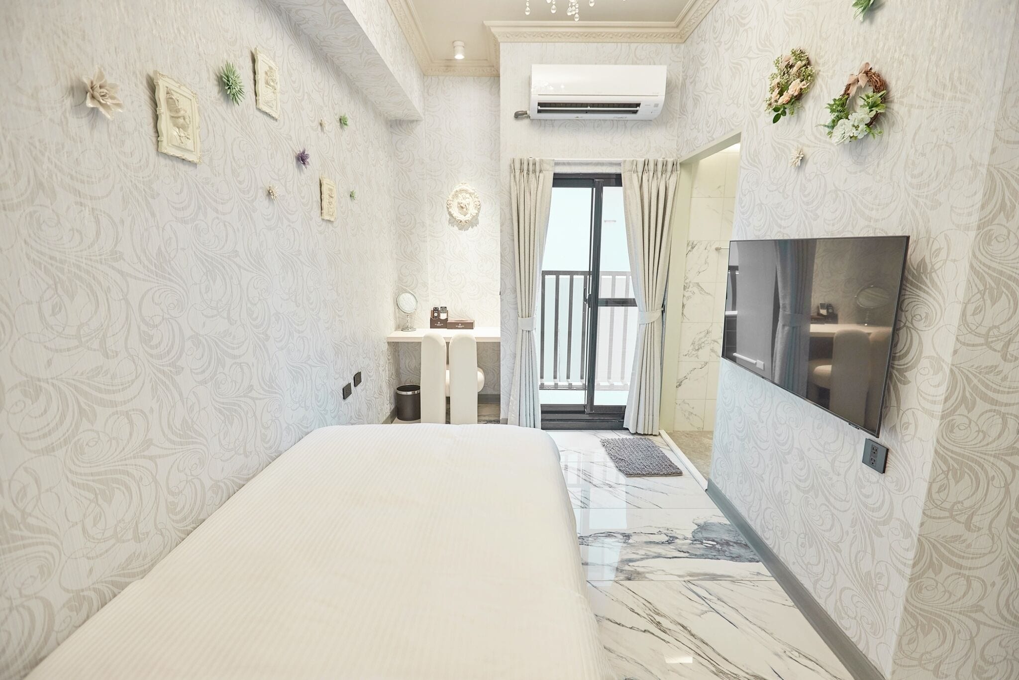 A hotel room with a bed, a TV, a small desk, and a balcony with curtains.
