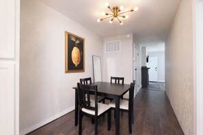 Cozy dining area with a wooden table and chairs, framed artwork, and a modern chandelier.