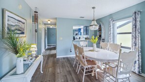 A dining area with a round table, white chairs, and a chandelier. There is a kitchen in the background with blue cabinets. - Cocoa Beach Vacation Rental - Walk to Pier! (Cocoa Beach)