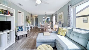 A modern living room with a sofa, ottoman, and a television on a shelf. - Cocoa Beach Vacation Rental - Walk to Pier! (Cocoa Beach)