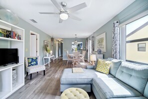 A modern living room with a sofa, ottoman, and a television on a shelf. - Cocoa Beach Vacation Rental - Walk to Pier! (Cocoa Beach)