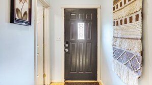 A hallway with a dark wooden door, a framed picture on the wall, and a macramé wall hanging. - Walkable Paradise: Downtown Puyallup Studio! (Puyallup)