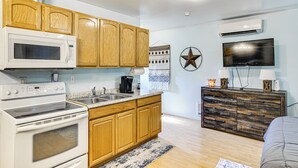 A modern kitchen with wooden cabinets, a microwave, stove, and a sink. There is a TV mounted on the wall and a decorative star on the wall. - Walkable Paradise: Downtown Puyallup Studio! (Puyallup)