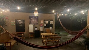 An outdoor seating area with wooden tables and benches, a hammock, and a sign for 'Nanda Parbat Hostal y Eventos'. - Nanda Parbat Hostal (San Rafael Cedros)