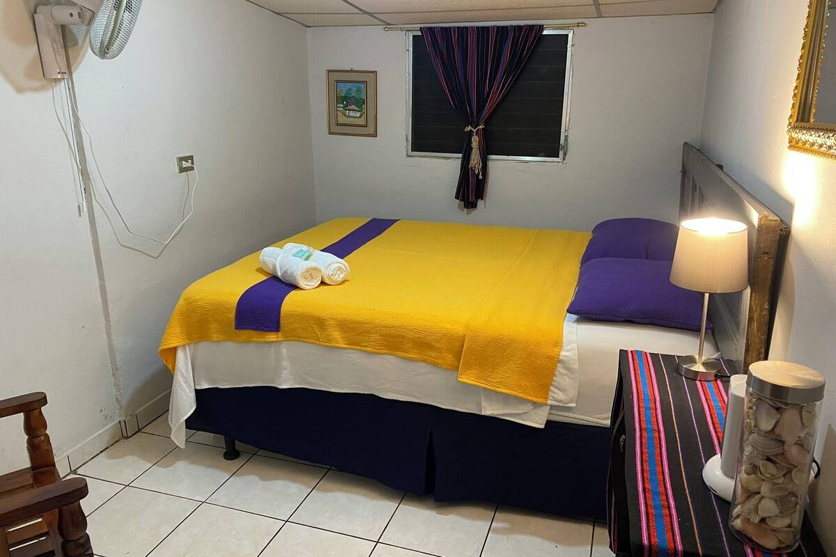 Habitació d'hotel amb un llit, una làmpada de nit, una taula petita amb un objecte decoratiu i una cadira.
