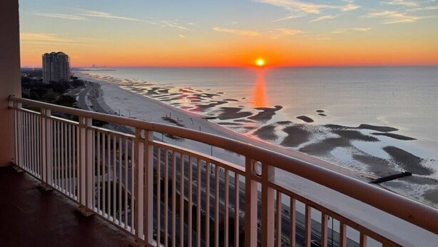 A balcony with a view of a beach at sunset. - Full Ocean View - SERENE SANDCASTLE 2 Bed/2 Bath (Gulfport)