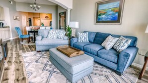 A living room with a blue sofa set, a coffee table, and patterned rugs. - Full Ocean View - SERENE SANDCASTLE 2 Bed/2 Bath (Gulfport)