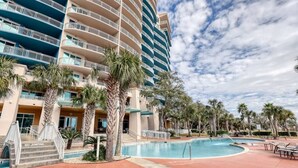 A hotel with multiple balconies, a swimming pool, and palm trees. - Full Ocean View - SERENE SANDCASTLE 2 Bed/2 Bath (Gulfport)