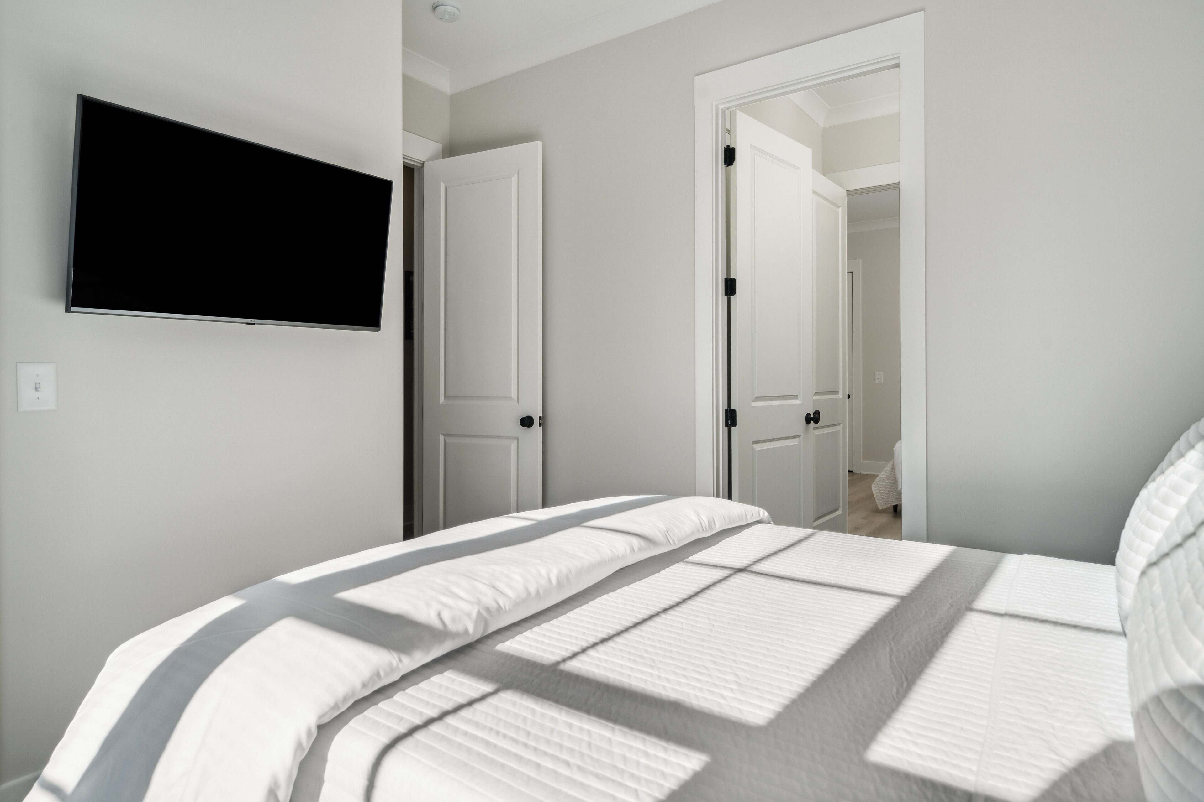 Un dormitorio con cama, televisión montada en la pared y dos puertas que dan a otras habitaciones.