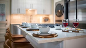 Une cuisine moderne avec des meubles blancs, un réfrigérateur en acier inoxydable et un coin repas doté d’un tabouret de bar.