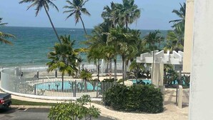 A beachfront view with a pool, palm trees, and a white fence. - Trinity Beach Apt (Rio Grande)