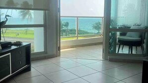 A modern living room with a large sliding glass door leading to a balcony with a view of the ocean. - Trinity Beach Apt (Rio Grande)