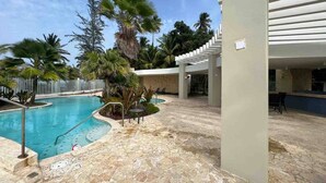 A pool area with a stone floor, palm trees, and a covered seating area. - Trinity Beach Apt (Rio Grande)