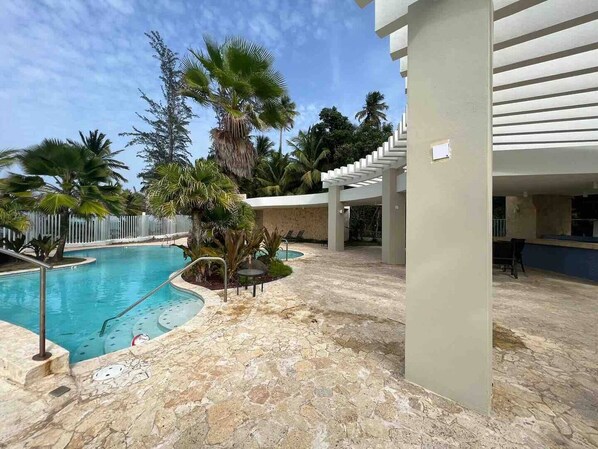 A pool area with a stone floor, palm trees, and a covered seating area.