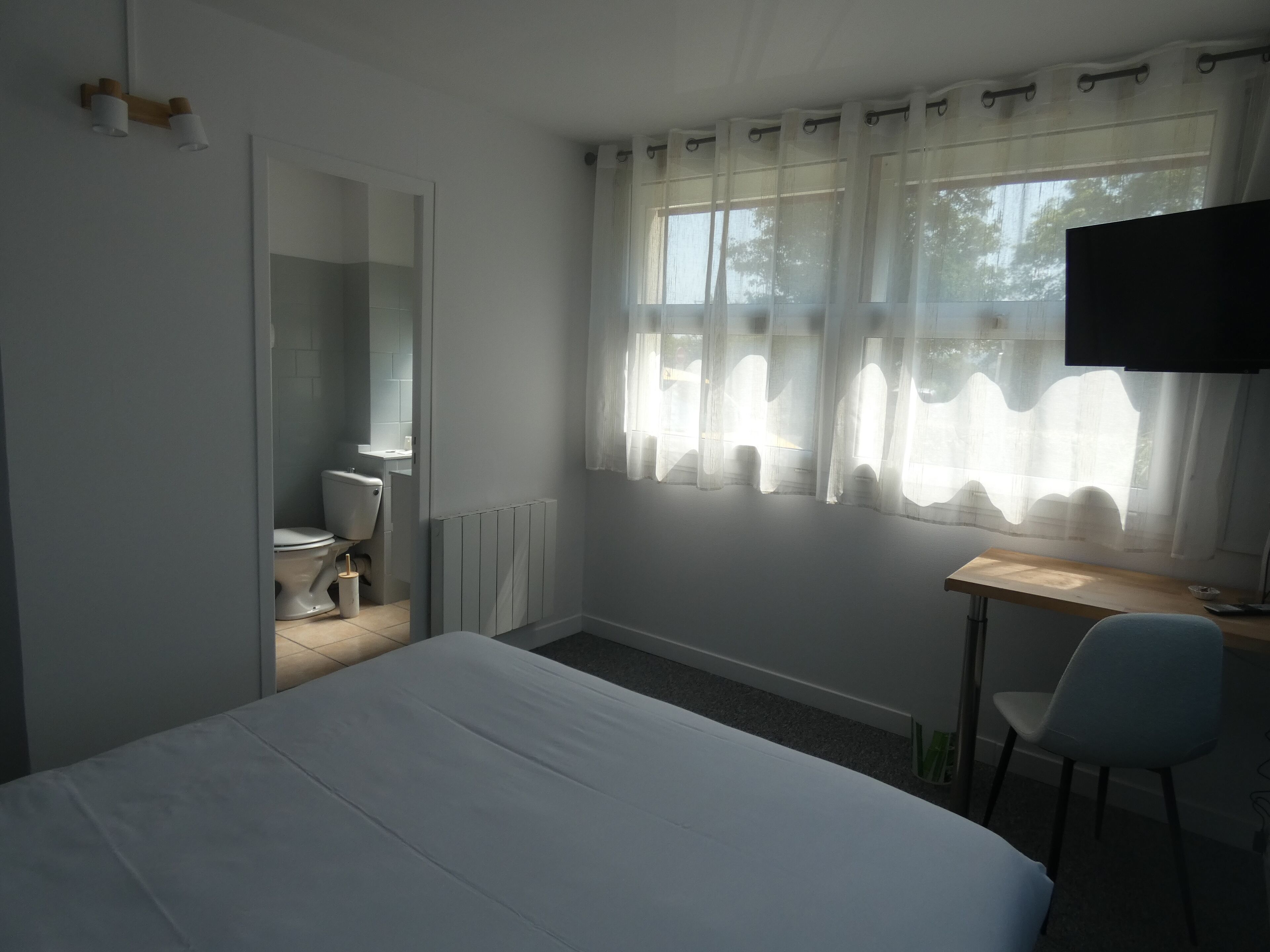 A room with a bed, a desk, a chair, a television, and a window with curtains.