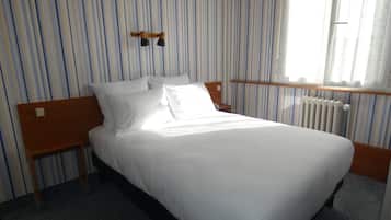 Une chambre d’hôtel avec un lit, une tête de lit en bois, une table de chevet et une fenêtre avec des rideaux.