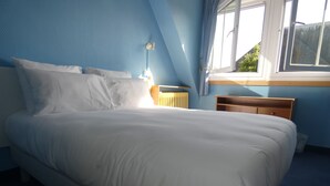 Un dormitorio con una cama grande, una mesita de noche, una lámpara y un ventanal con cortinas.