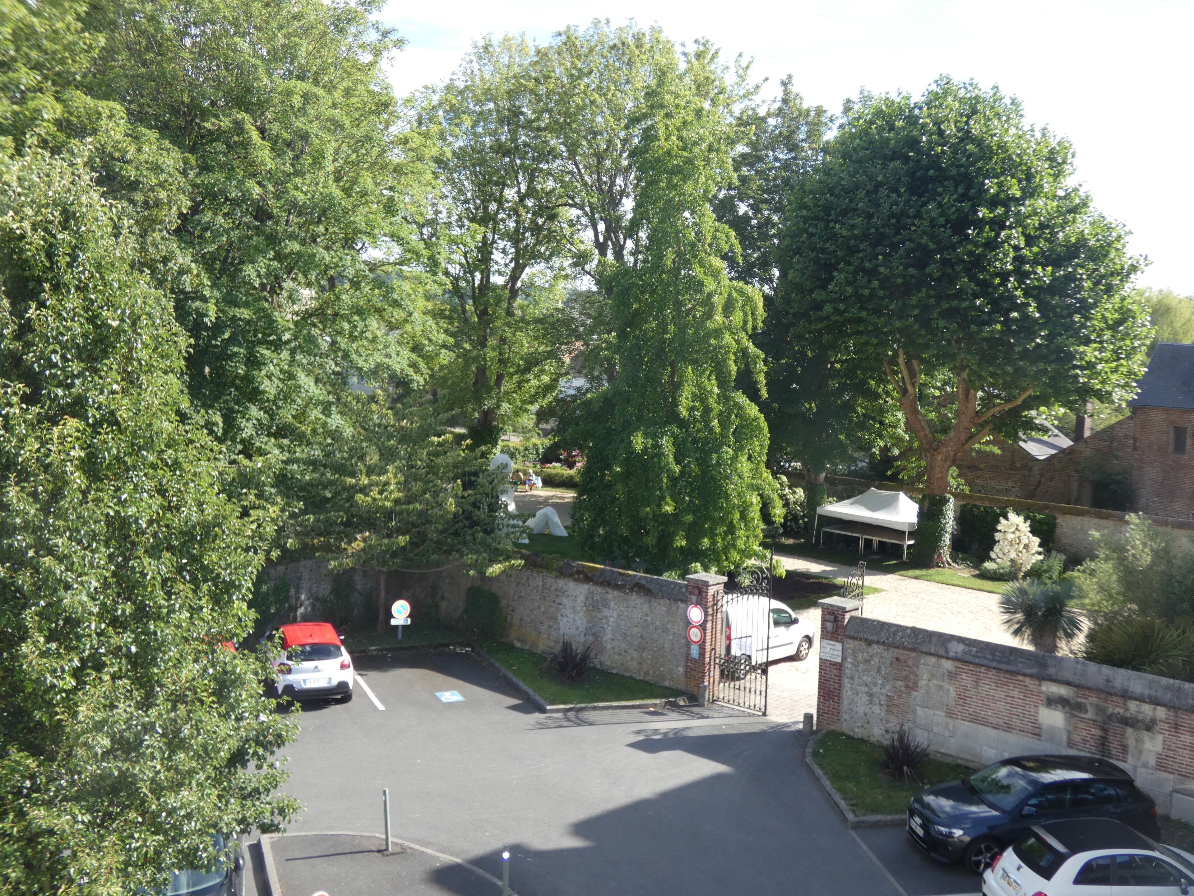 A parking area with cars, a gated entrance, and surrounding greenery.