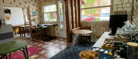 Un rincón acogedor para desayunar, con una mesa de madera, una tabla de cortar con pan y un bufé con platos y tazones.