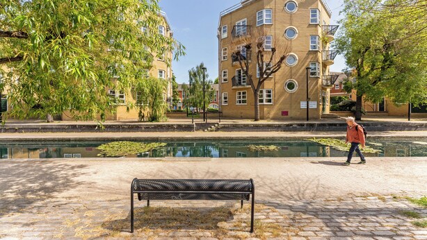Un parc avec un banc, un étang et un bâtiment doté de nombreuses fenêtres et de balcons.