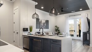 A modern kitchen with a central island, dark cabinetry, pendant lighting, and a view to the outdoors. - 3 Bedroom, Main Level - ADA  (Helena)