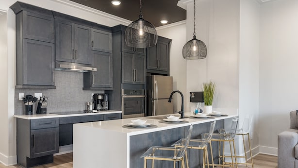 A modern kitchen with dark gray cabinets, stainless steel appliances, a large island with bar stools, and pendant lighting. - 3 Bedroom, Main Level - ADA  (Helena)