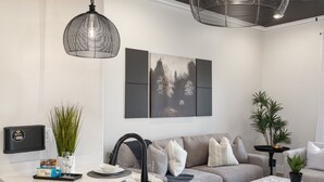 A modern kitchen with a built-in sink, a dining area with a white table and chairs, and a grey sofa in the living area. - 3 Bedroom, Main Level - ADA  (Helena)