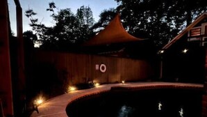 A swimming pool with a curved edge, surrounded by a wooden deck and a covered area with a pointed roof. - Relaxing garden cottage with sauna
 (Shreveport)