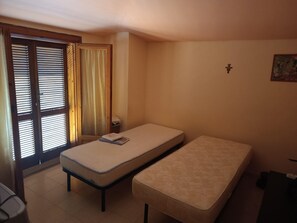 A small, single-bed room with a window, a curtain, a cross on the wall, and a small table. - Apartment near the sea in Tropea (Tropea)