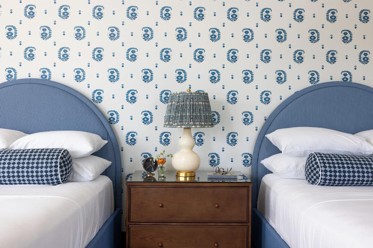 A bedroom with two beds, a nightstand, and a lamp.