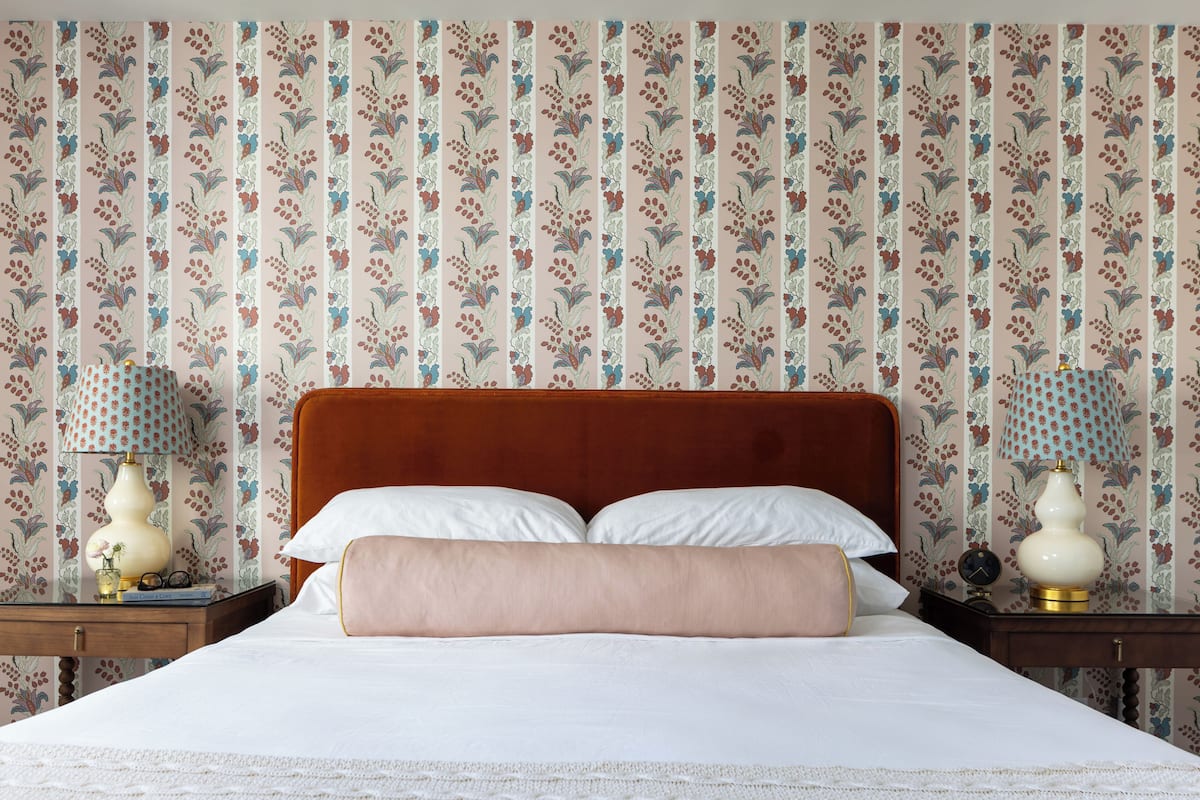 A neatly made bed with a wooden headboard, two bedside tables with lamps, and floral wallpaper.