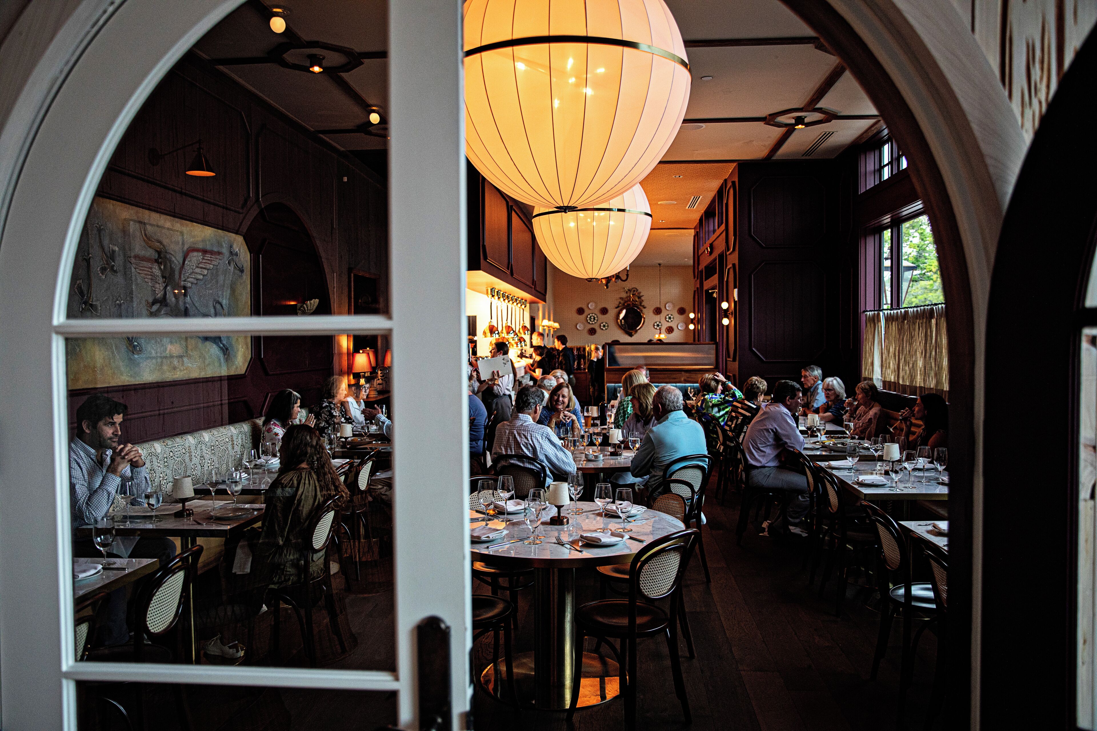 En restaurantindretning med runde borde, stole og hængende lamper.