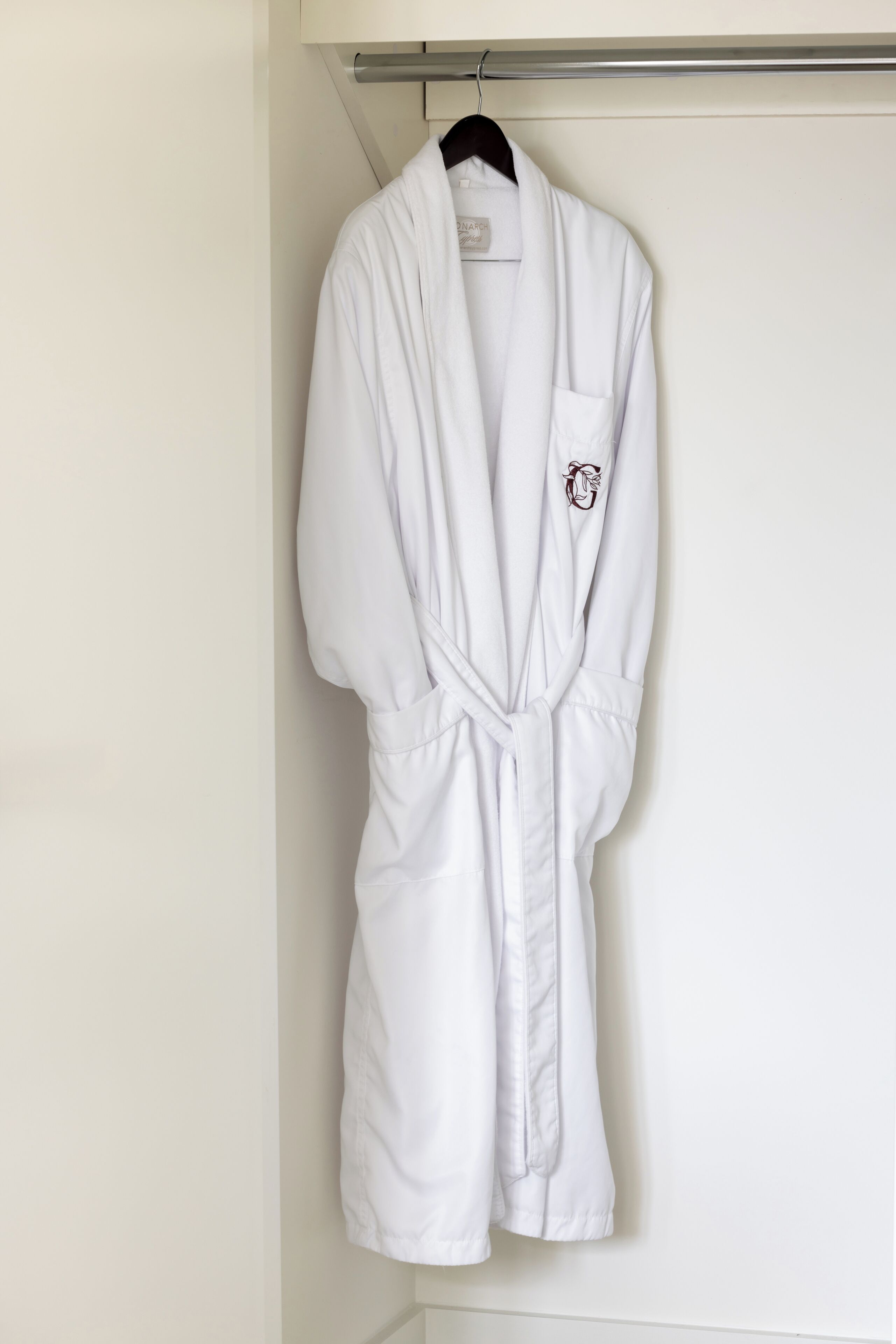 A white bathrobe hanging on a metal rod in a bathroom.